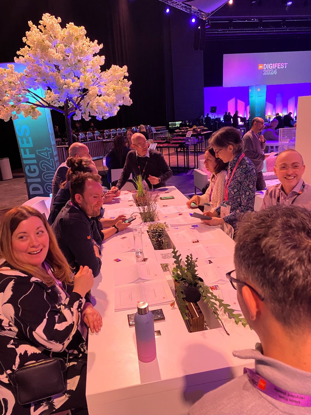 People from the digital storytelling community smiling and sitting around a modern, white table at a conference.