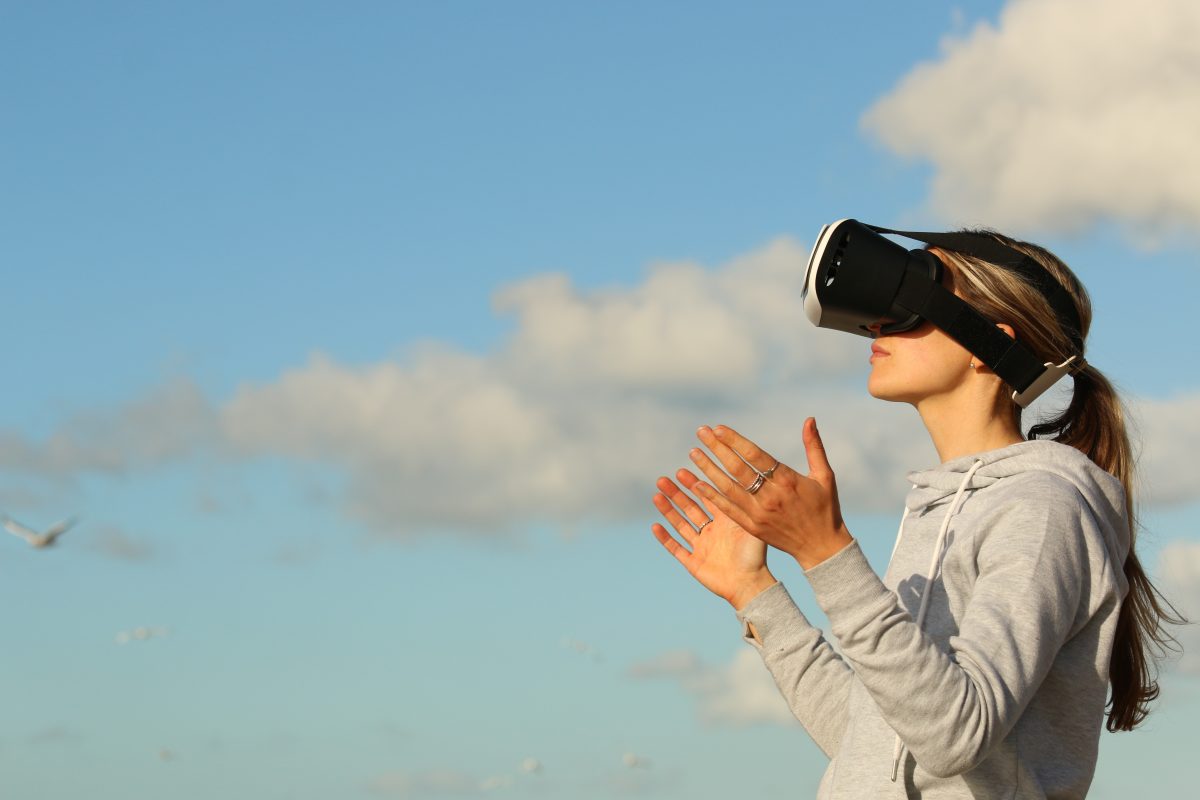 Woman wearing a VR headset photograohed against a blue sky with clouds