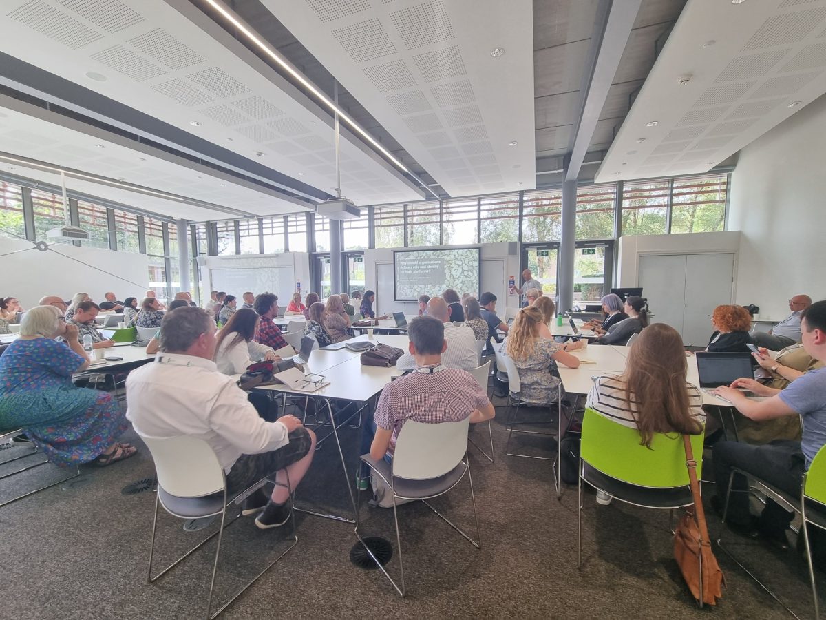 People sitting around tables in bright, modern teaching space, listening to a presentation at the ALTC23 conference