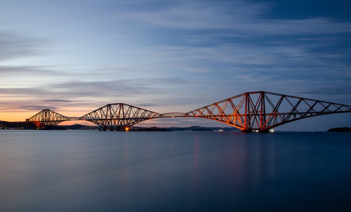 The Forth Bridge, a red cantilever structure spans the estuary mouth at dusk