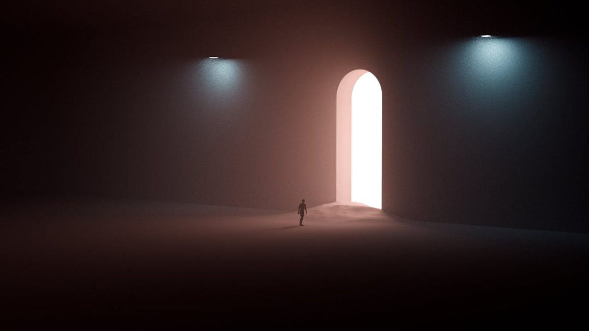 A dreamlike picture of a lone figure in darkness approaching a huge doorway from which light floods