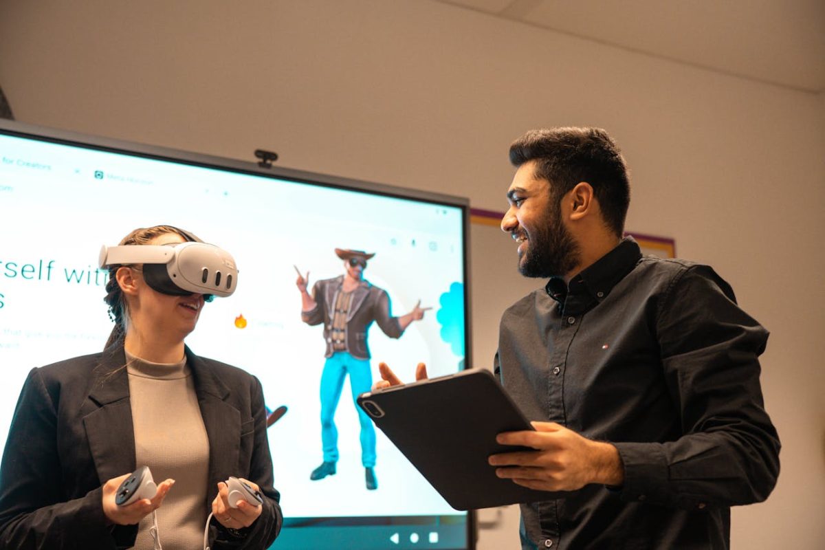 woman using virtual reality headset, in the background is a virtual avatar on screen and to the right is a man guiding her through the virtual reality experience
